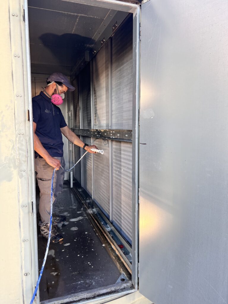 Man wearing mask cleaning air ducts inside metal air vent system using specialized vacuum equipment