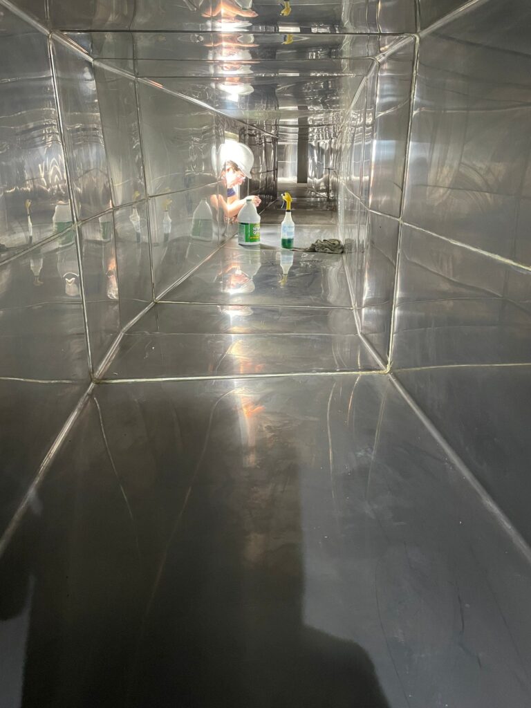 Technician cleaning air ducts in a reflective metal enclosure, ensuring indoor air quality and HVAC efficiency.