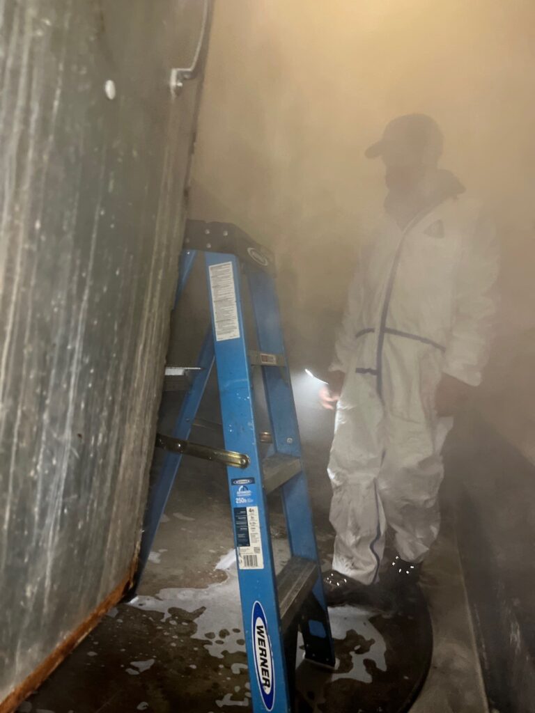 Technician cleaning air ducts in tight space using a Werner ladder and proper safety gear