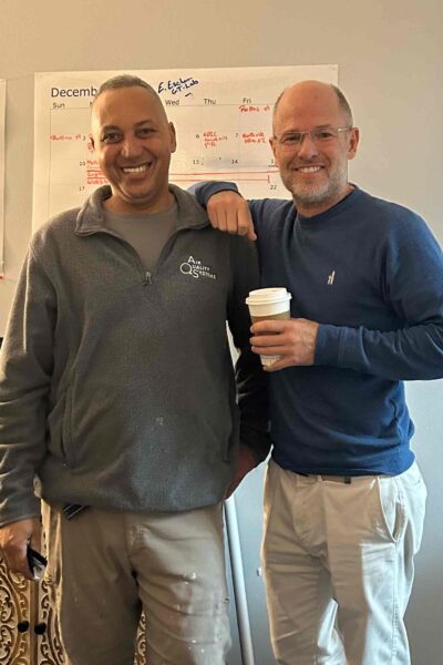 Two smiling HVAC technicians standing together holding a coffee cup, on a job site