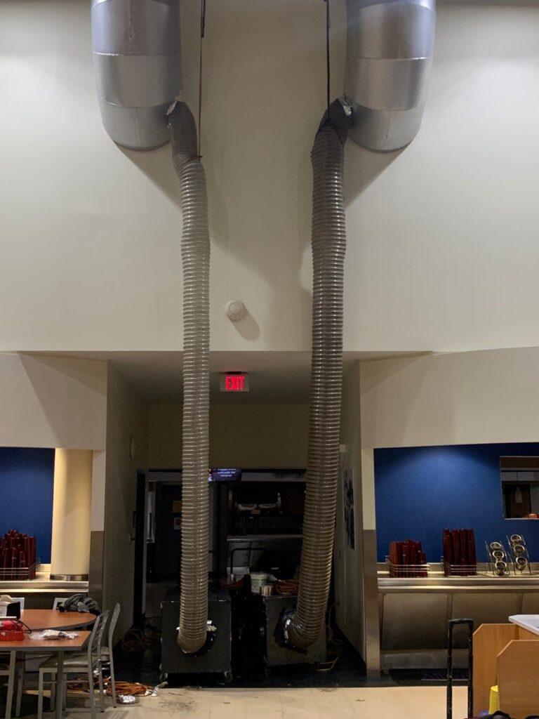 Air ducts with flexible hoses extending from ceiling in commercial kitchen, ready for cleaning services.
