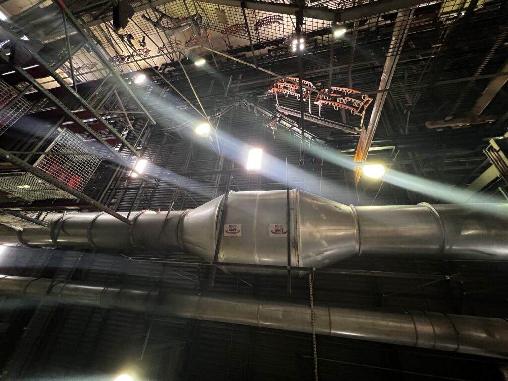 Large industrial ductwork inside a warehouse, lit by overhead lights, for commercial air duct cleaning services.