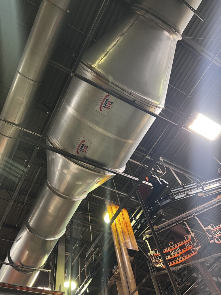 Shiny metal air ducts in industrial building, showcasing professional commercial duct cleaning services