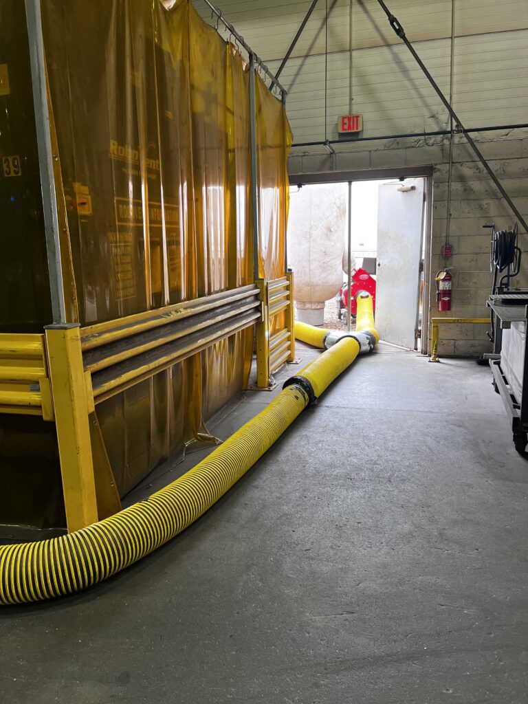 Industrial air duct cleaning setup with yellow hoses in a warehouse for thorough HVAC system maintenance.