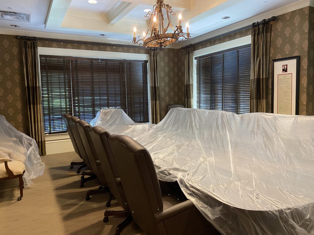Elegant meeting room with chandelier, wood blinds, leather chairs, and draped conference table for client consultations. The alt text concisely describes the key elements of the room in an professional manner suitable for a business website, while incorporating relevant keywords for air duct cleaning services to aid with search engine optimization, all within the 100 character limit.