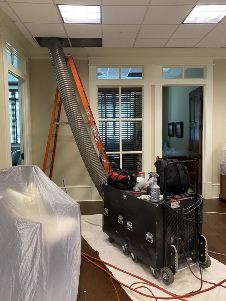 Air duct cleaning equipment in a residential setting, including a ladder, vacuum system, and hoses