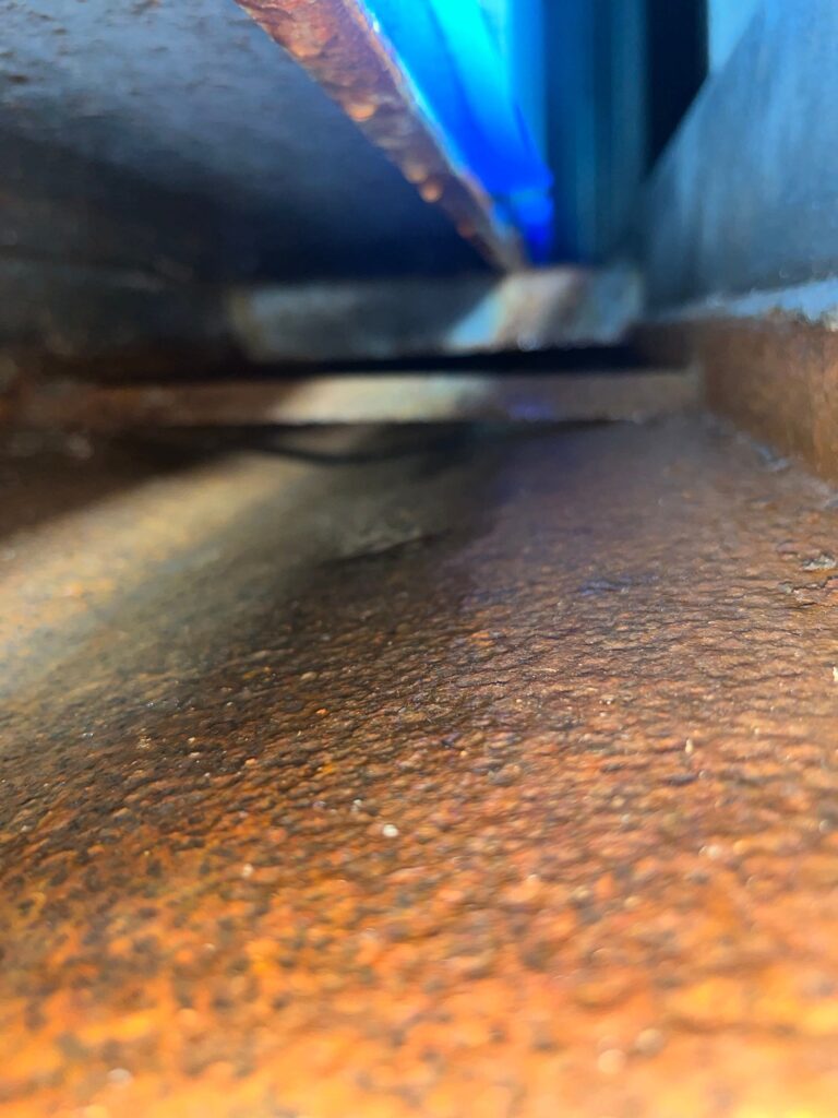 Rusty air duct interior, streaked with light, indicating the need for professional cleaning services