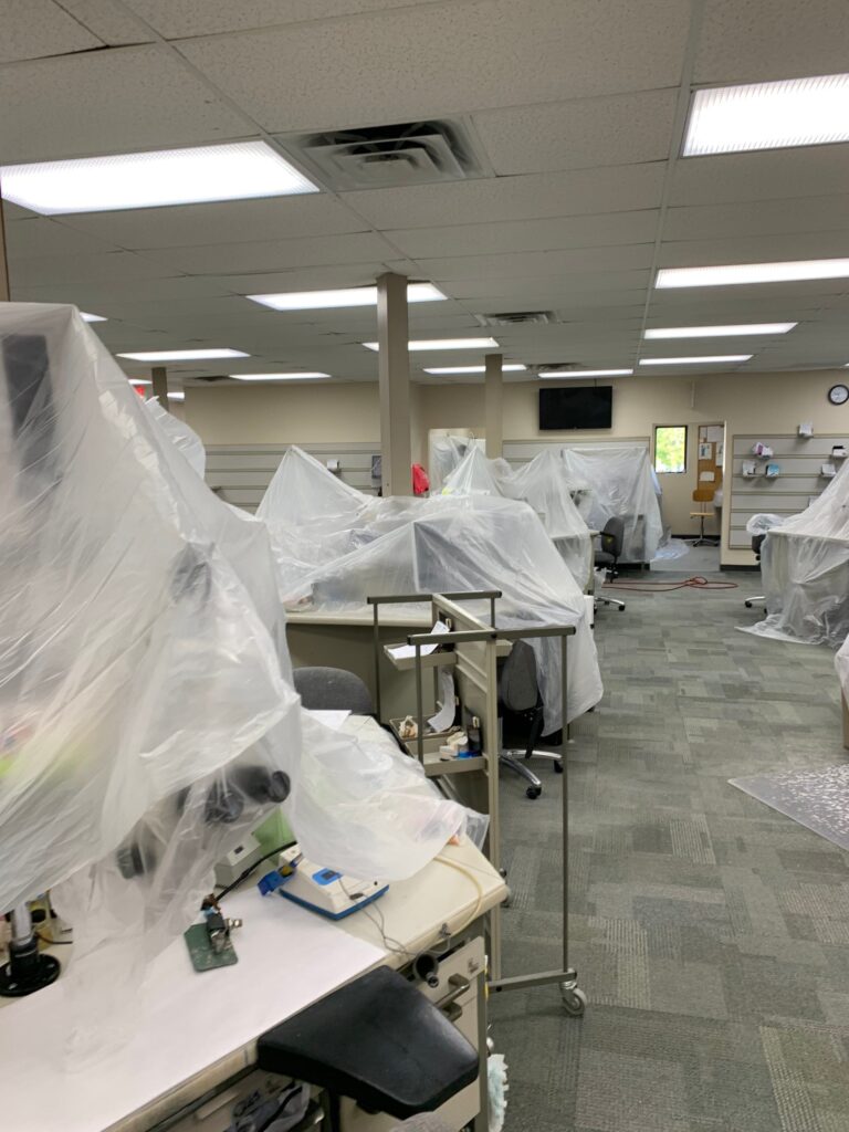 Commercial air duct cleaning workspace with equipment, plastic sheeting, and workstations in a large room.