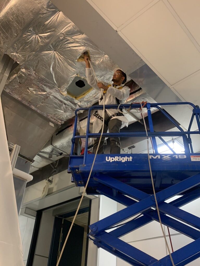 HVAC technician cleaning air ducts in ceiling using UpRight MX19 lift for improved indoor air quality