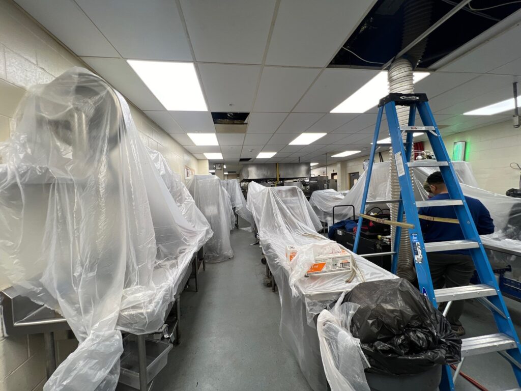 Plastic-wrapped HVAC equipment awaits installation in a commercial building by technicians on ladders, ensuring top air quality.
