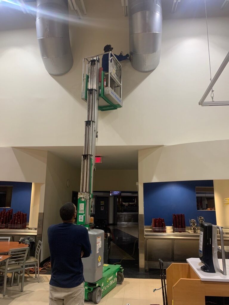 HVAC technician using a lift to clean and maintain commercial building air ducts for optimal air quality.