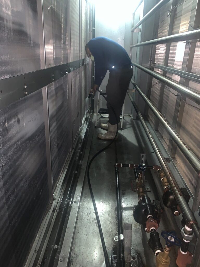HVAC technician cleaning commercial air ducts in a narrow metal enclosure using specialized equipment