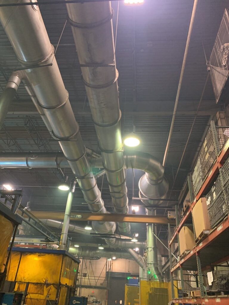 Industrial ventilation system with metal ducts, pipes, and lights in a large warehouse or factory setting